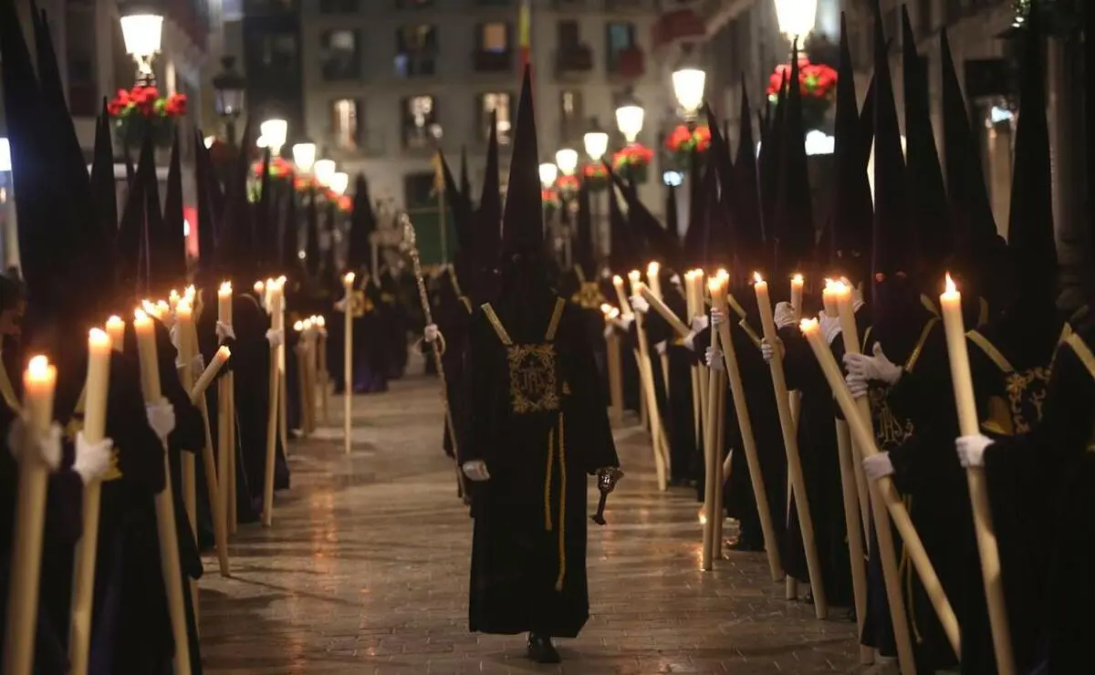 Mayordomo entre nazarenos con velas por Calle Larios
