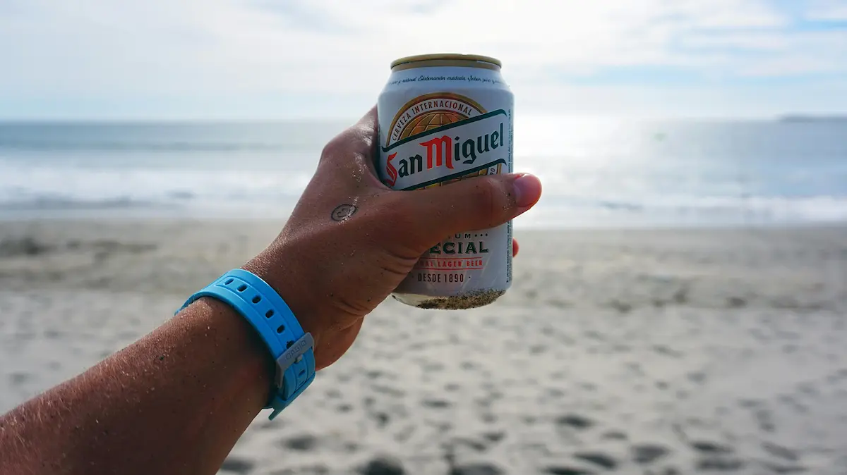 Une main tient une canette de bière San Miguel sur une plage de Malaga