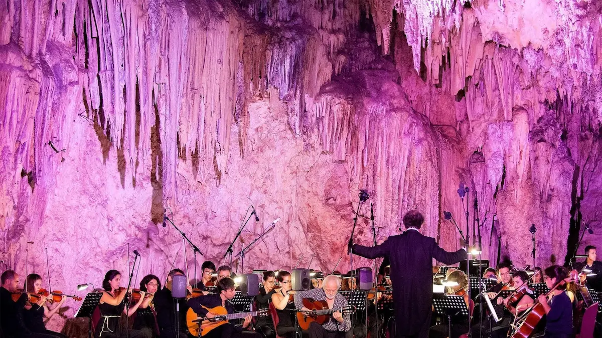 Orquesta tocando en el iluminado Festival de Música de las Cuevas de Nerja, rodeada de estalactitas